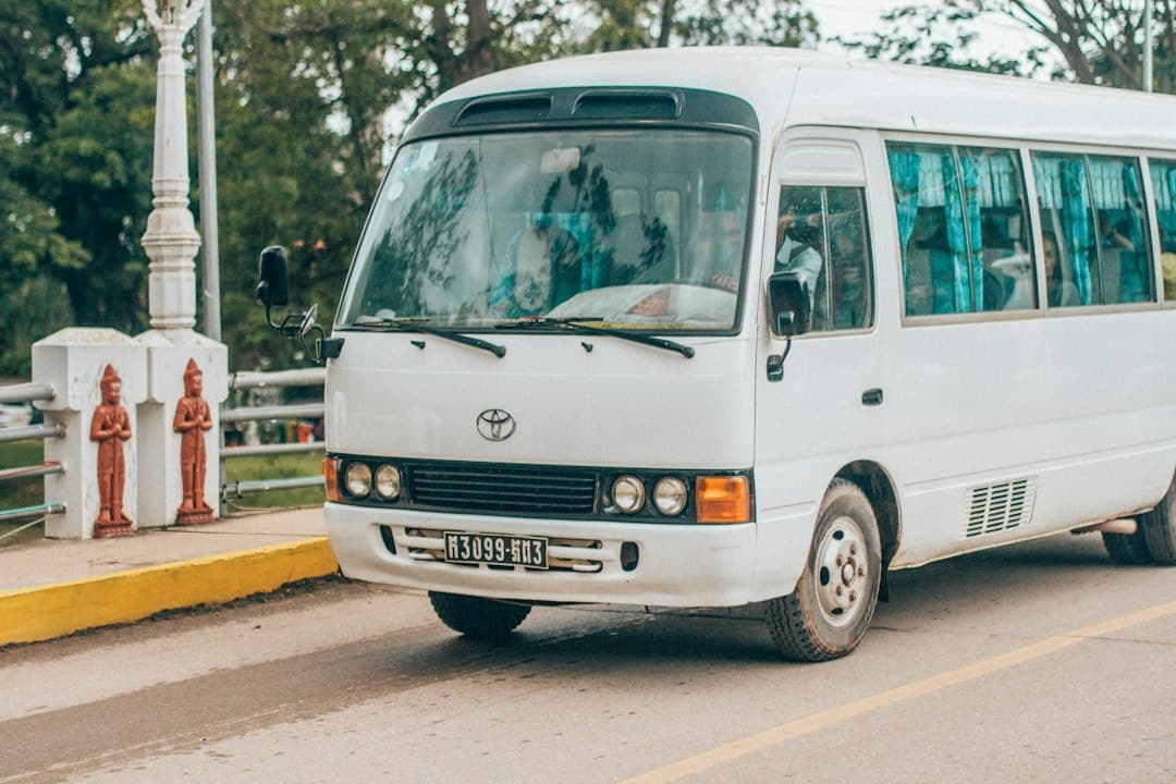 White Toyota minibus at a Cambodian roadside stop with Buddhist statues and temple structures.