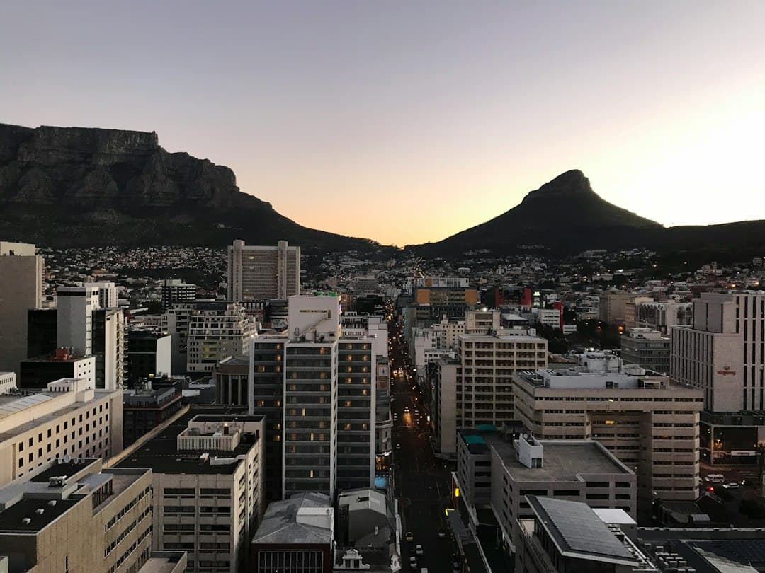 Stadsgezicht van Kaapstad bij zonsondergang, gezien vanaf een hoog balkon, met de Tafelberg en de Duivelspiek zichtbaar.