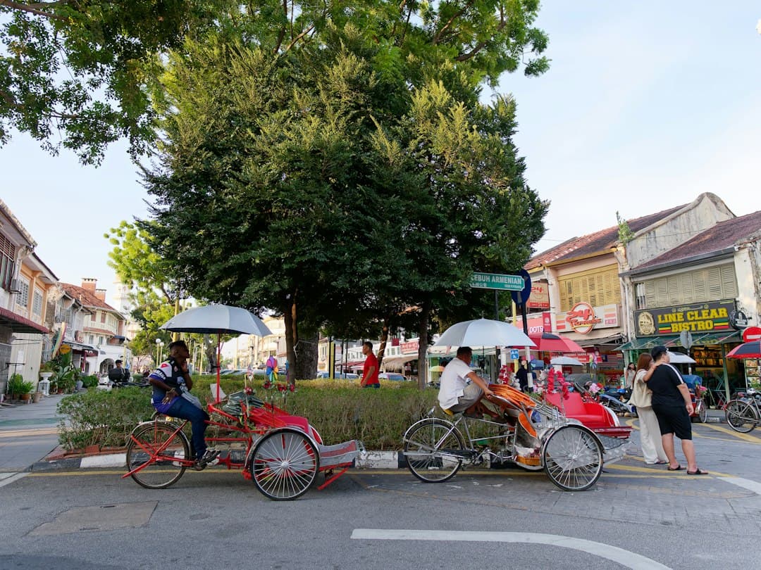 Colonial houses and a shaded street in George Town, Penang, with local rickshaws and pedestrians.
