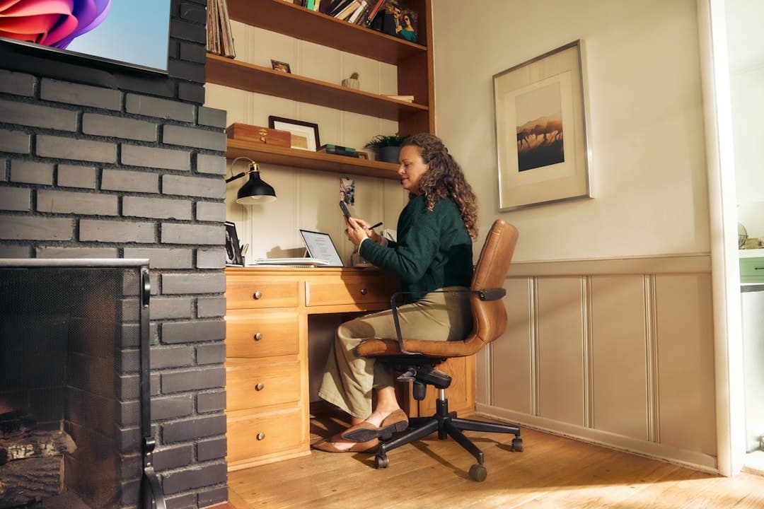 Una donna che lavora a distanza da un ufficio domestico, consultando il suo telefono mentre utilizza un computer portatile.
