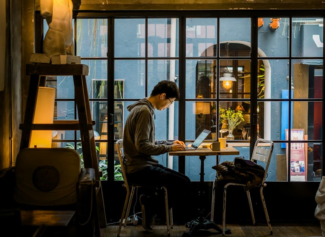 Remote worker typing on a laptop at a café table by a window overlooking the city